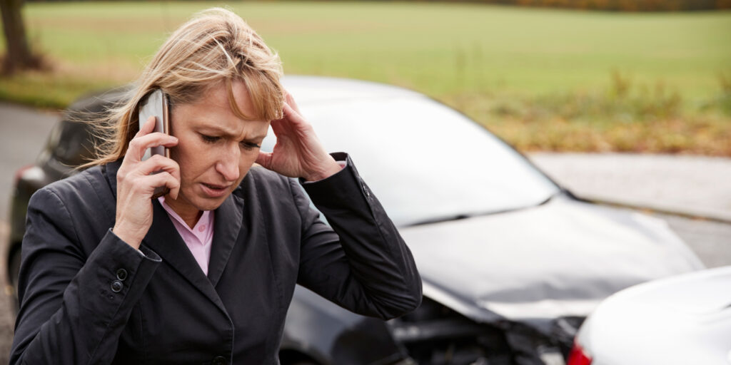 Distressed woman holding her head and calling for help on a smartphone beside two damaged cars after a rideshare collision in Florida.