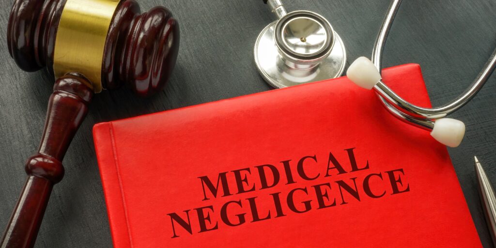 Sober, professional arrangement on a dark wooden surface featuring a red book labeled 'Medical Negligence,' a wooden legal gavel, and a physician's silver stethoscope. Visual asset supports medical malpractice litigation, hospital negligence claims, and healthcare provider accountability under Florida law in Coral Springs and Fort Lauderdale.