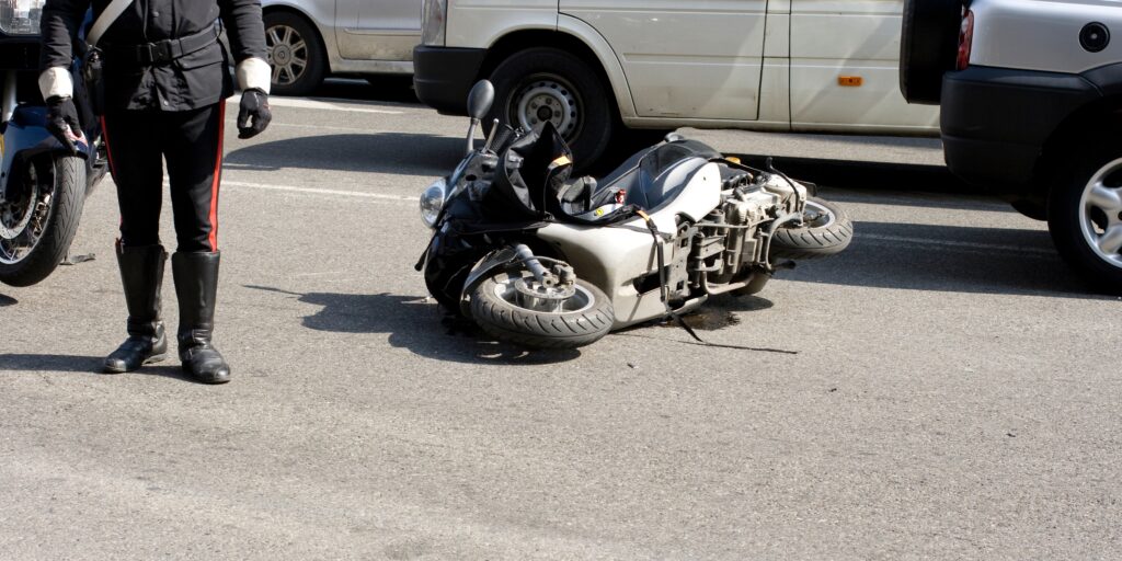 Law enforcement officer standing next to a damaged scooter lying on its side following a traffic collision in South Florida.